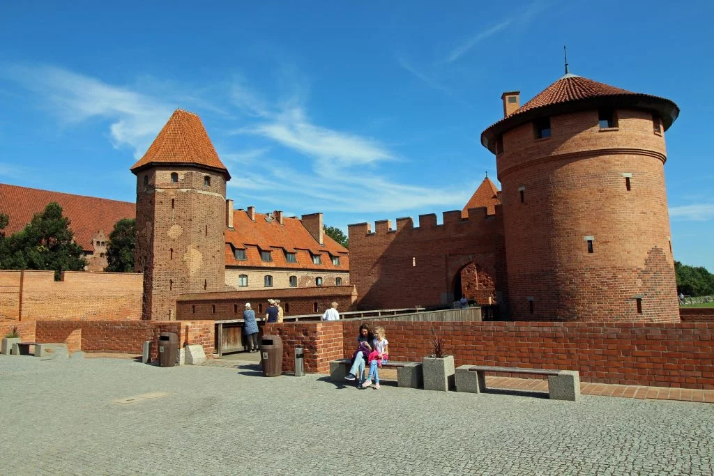 Two Malbork castle towers appear infront of each other separate by the bridge with tourists walking