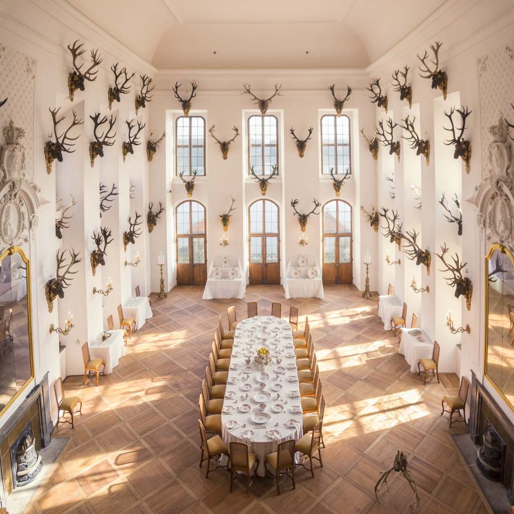The antler room inside Moritzburg castle. Lots of antlers hanging on the tall white walls with a huge dinning table in the center.