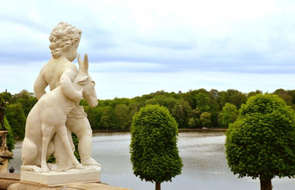 The statue of a boy and a goat looking into the horizon from the balcony of Moritzburg castle with lots of greenery around.