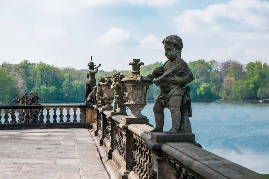 A lineup of statues on the balcony of Moritzburg castle with the lake and trees in the light background.