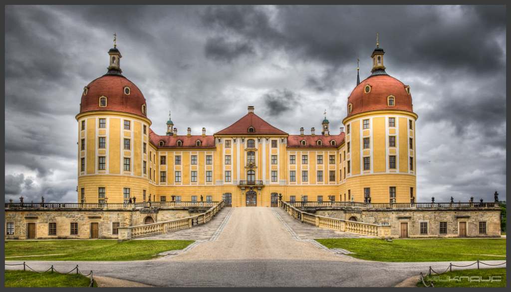 The beautiful, highly symmetrical architecture of the Moritzburg castle with dark clods in the sky.