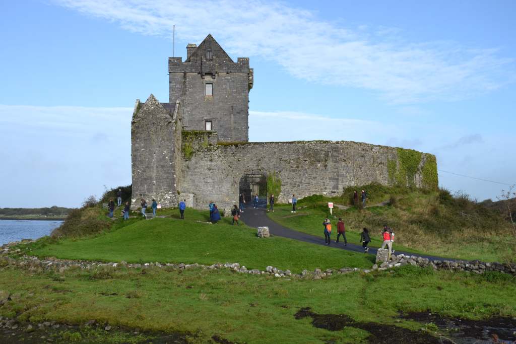 The entrance and stone walls of the Dunguaire castle and tourists on their way inside.