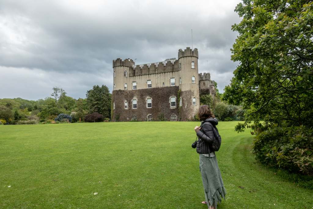 A beautiful view of Malahide Castle from the grounds. surrounded by green trees, bushes and grass.