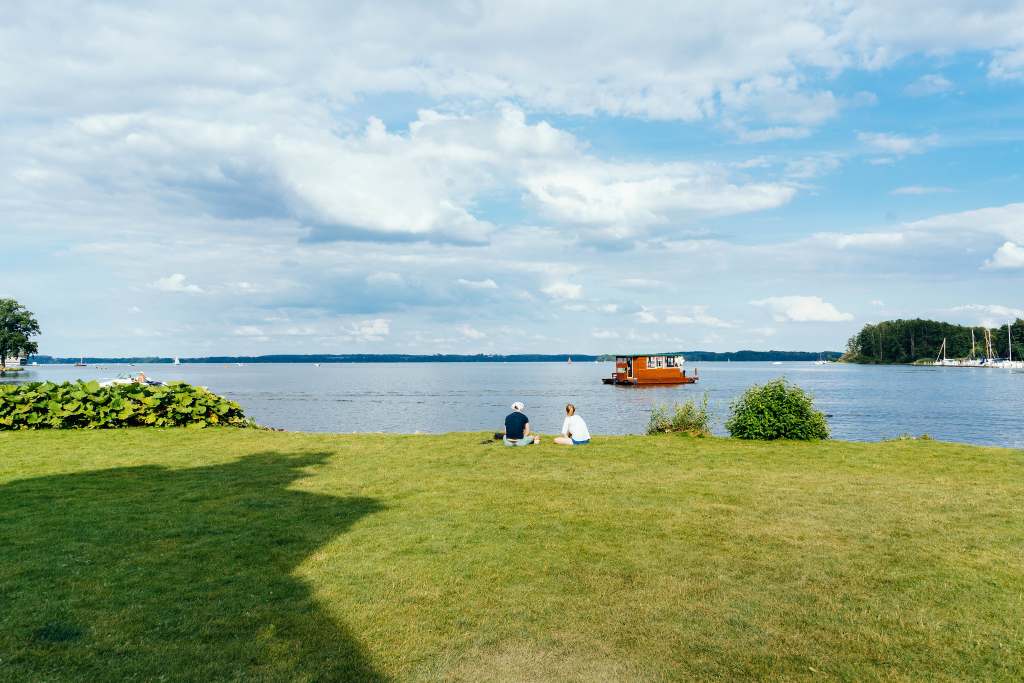 A view of the sprawling grounds surrounding the Schwerin castle near the lake with a boat and two people sitting.