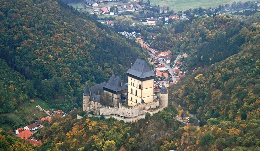 An aerial view of the Karlštejn Castle that highlights its significant geographical position, the road that leads to it, and the town at its base.