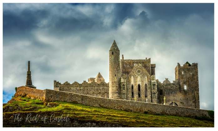 The sideview of Rock of Cashel Castle from a distance with dark clouds in the horizon.