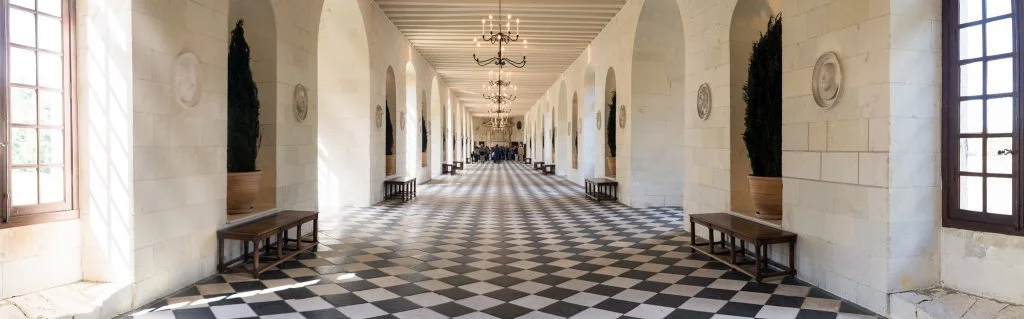 The panoramic view of Château de Chenonceau's hallway interior lined up with chandeliers
