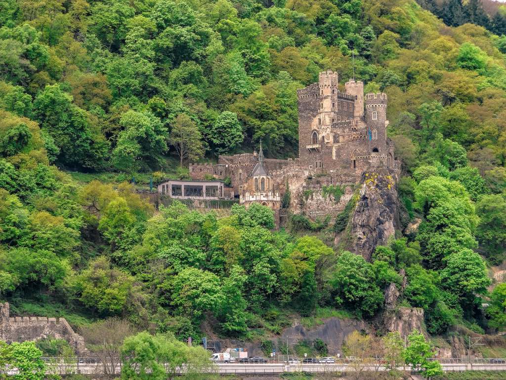 The scenic view of Rheinstein Castle from afar surrounded by greens and the road can be seen from below. 