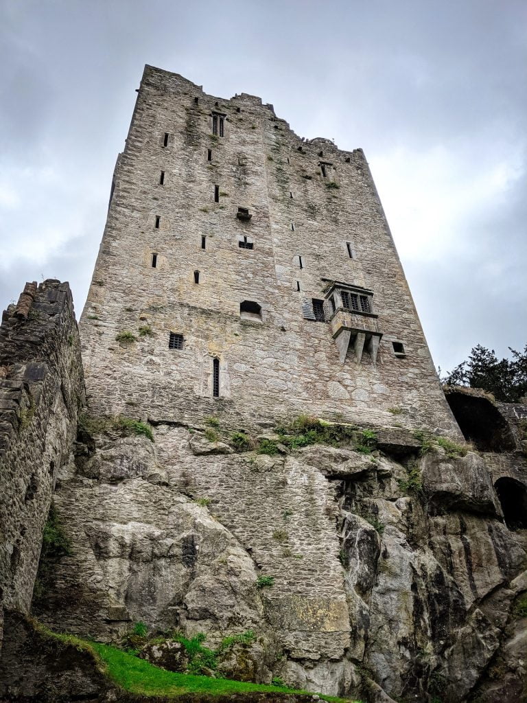 A full view of the imposing tower of Blarney Castle set on top of a rocky outcropping.