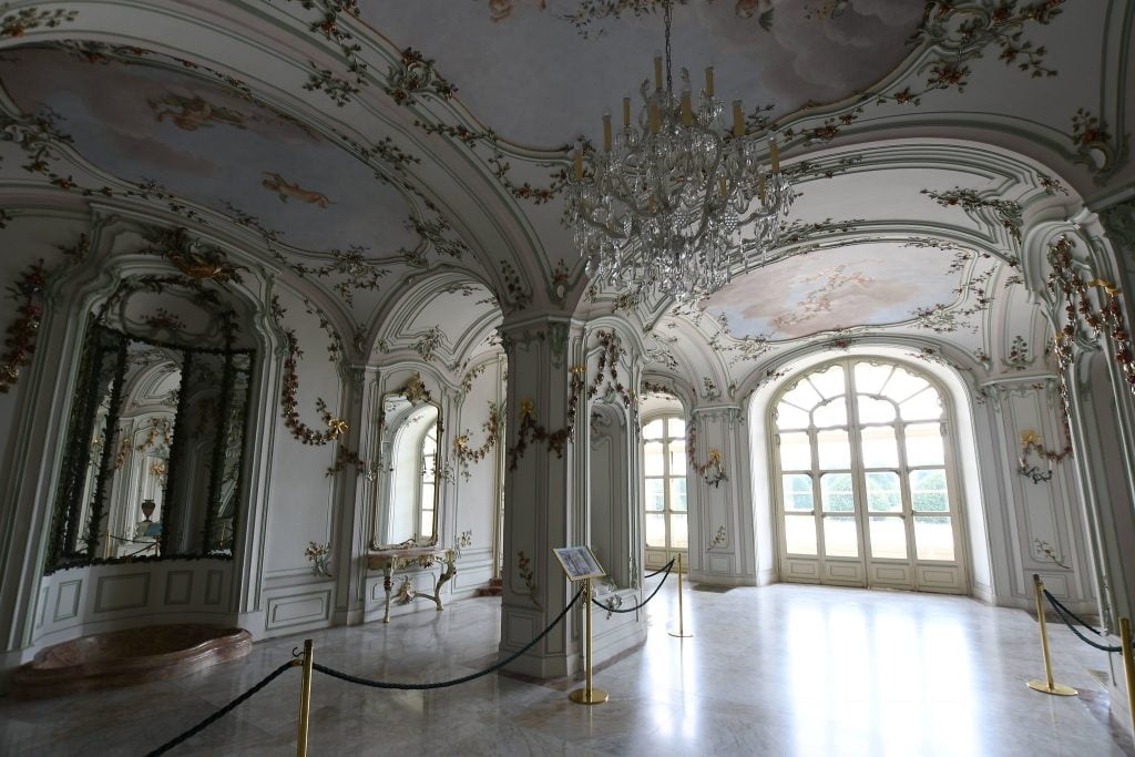 The beautiful interior of Esterhaza Palace with white walls, some gold details and a chandelier.