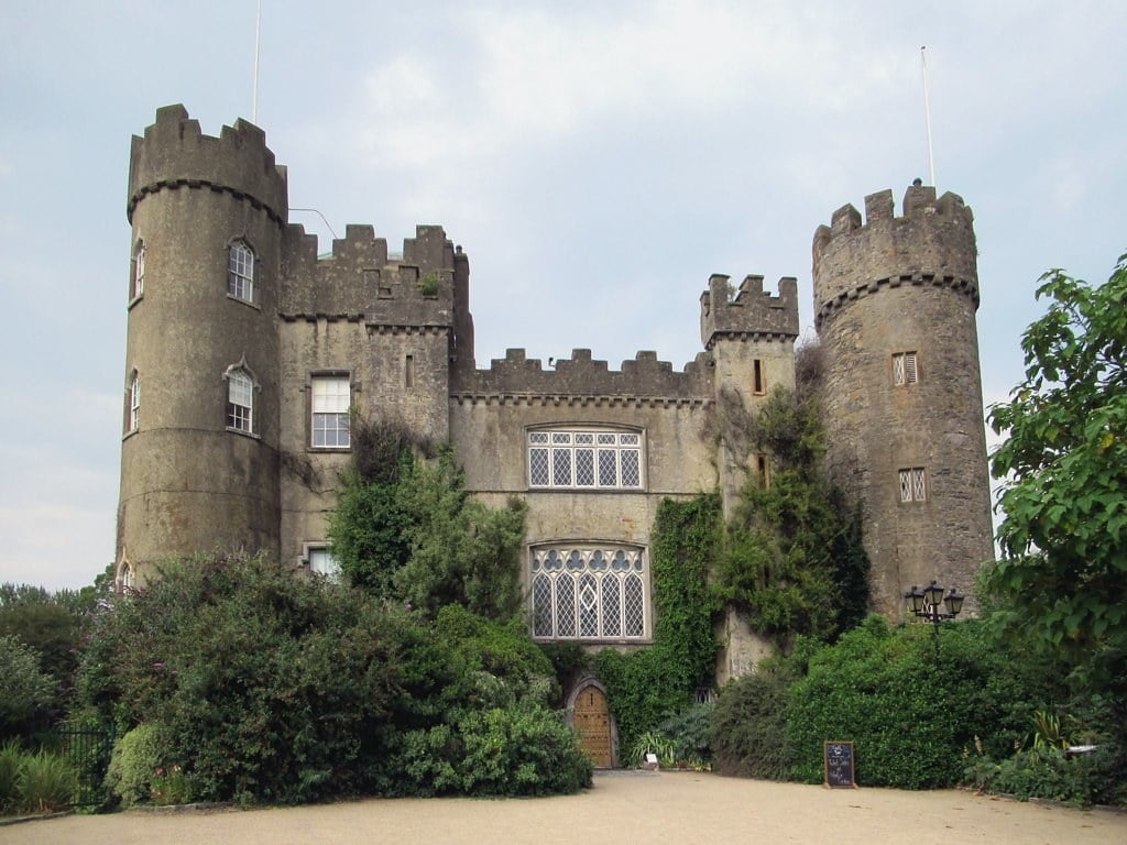 The front view of Malahide Castle where the entrance door is surrounded by green big bushes.