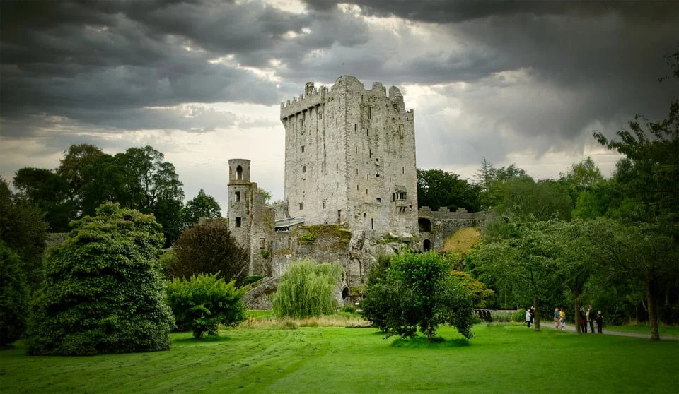top 10 castles to visit in ireland The tower of Blarney Castle surrounded by trees with view visiting tourists spotted.