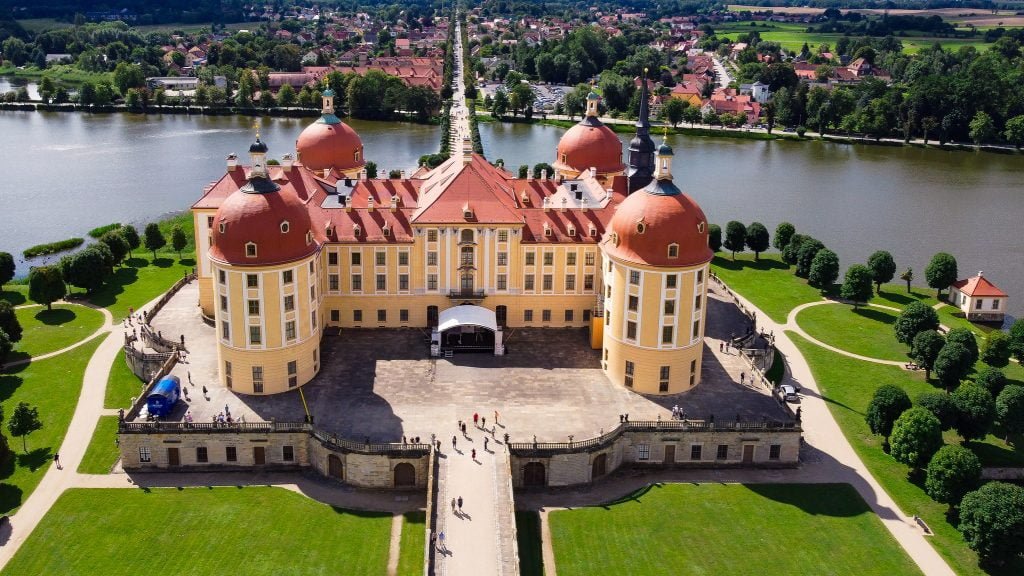 The aerial view of the beautiful Moritzburg Castle with a view of the river behind and the green grounds outside the castle.