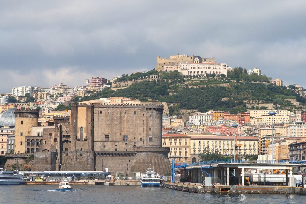 Side view of Castel Nuovo rfoma across the water surrounded by buildings.