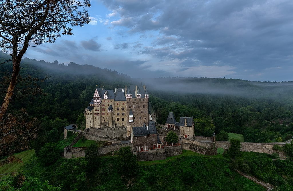 The picturesque view of Eltz Castle from afar.  with view of trees and mountains.
