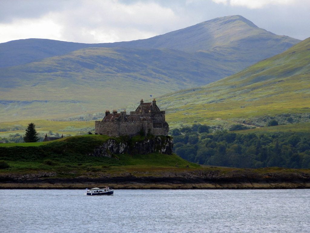 Duart Castle against the Scottish Highlands with a passing ferry in the foreground.